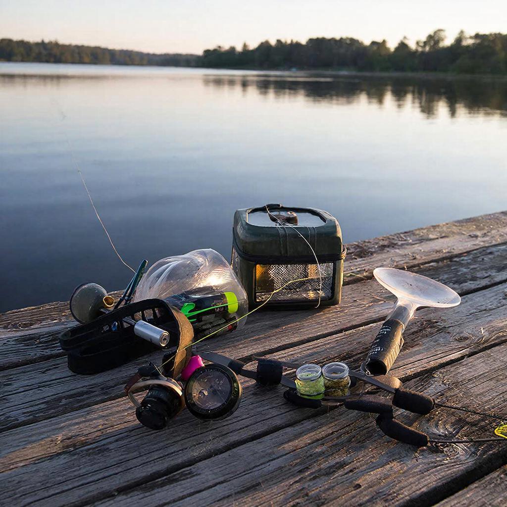 Практичный набор насадок и прикормки на деревянном настиле у озера на рассвете: бойлы, кукуруза, тигровый орех, пеллетс, зерновая смесь, червь и опарыш, без лишнего декора.