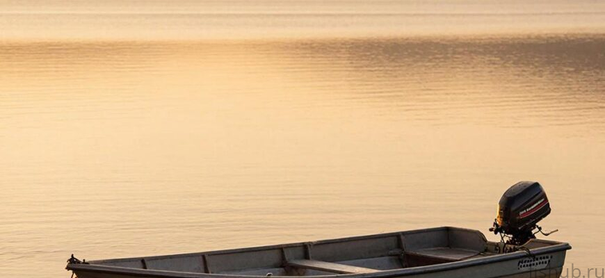 Вид на лодку с электромотором на спокойном озере во время заката.