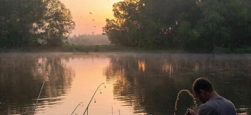 Рыбак готовит приманку из манной крупы на берегу тихого озера на рассвете, в туманной атмосфере и мягких красках восходящего солнца.